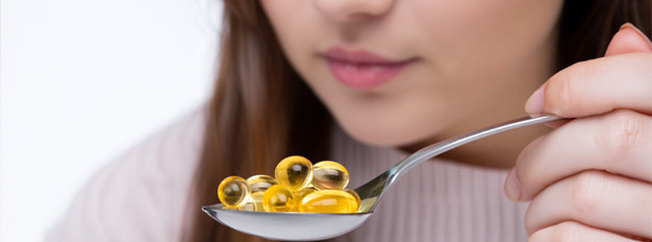 Woman holding a spoon of golden omega-3 softgel capsules near her mouth, SANUSq Health supplements